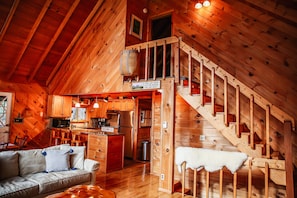 Cozy cabin interior with a comfortable sofa, wooden staircase, and a small kitchen area.