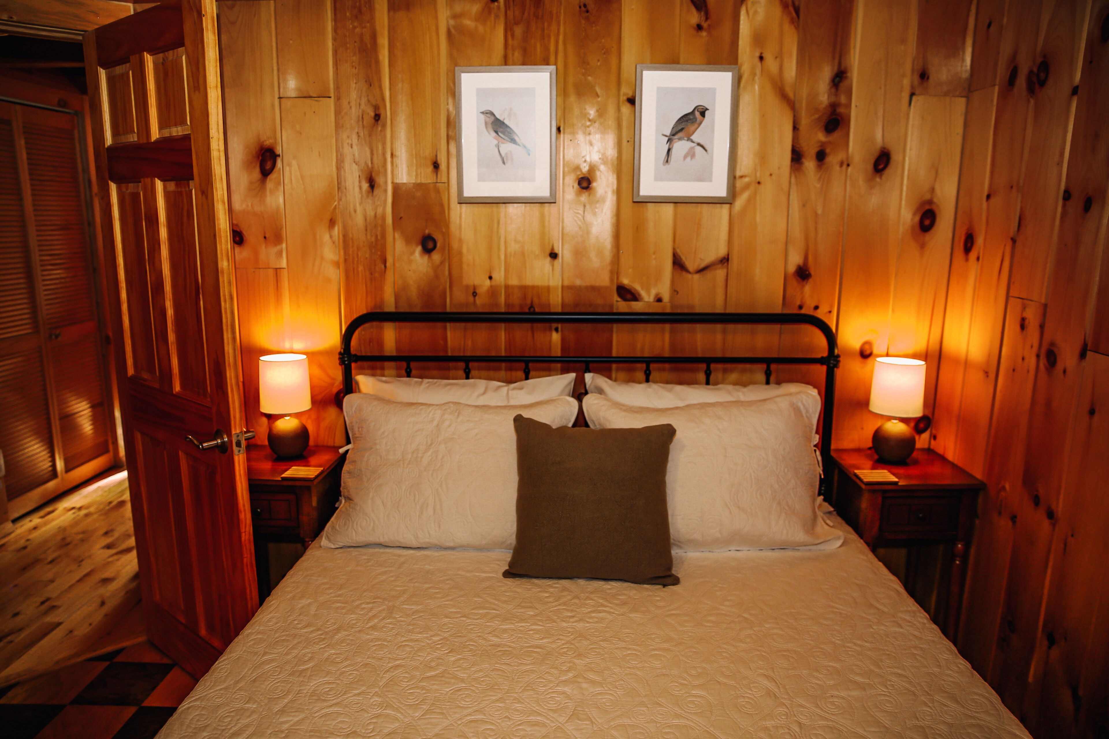 Una habitación con paneles de madera, una cama, dos cuadros en la pared y dos lámparas de noche.