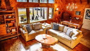 Un interior de cabaña acogedor con paredes de madera, ventanas amplias, una araña y una zona de comedor.