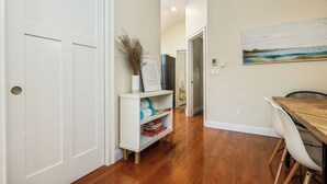 A hallway with a white door, a white console table with decorative items, a painting on the wall, and a dining area with a wooden table and chairs. - The Nest-Cozy Retreat Near Portsmouth +Ogunquit, Full kitchen, close to every... (York)