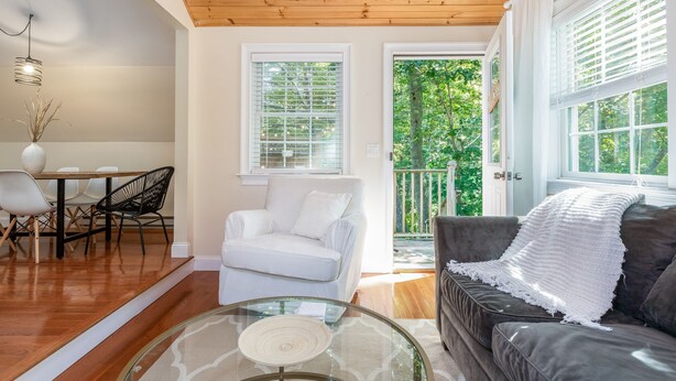 A modern living room with a wooden ceiling, a glass coffee table, a white sofa, a dark grey sofa, and a dining area with a white table and chairs. - The Nest-Cozy Retreat Near Portsmouth +Ogunquit, Full kitchen, close to every... (York)
