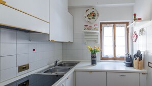 Eine kleine Küche mit weißen Schränken, einer Spüle und einem Fenster mit Spitzenvorhängen.