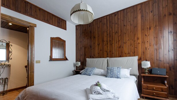 Ein Schlafzimmer mit einer holzverkleideten Wand, einem Bett mit weißer Bettwäsche, zwei Nachttischen mit Lampen und einer Hängelampe.