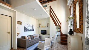 Ein modernes Wohnzimmer mit einer Couch, einem weißen Sessel, einem Fernseher und einer Treppe, die in eine obere Etage führt.