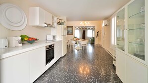 Een moderne keuken met witte kasten, een zwart beklede vloer en een eethoek met witte stoelen en een tafel.
