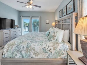 A bedroom with a bed, a television, a ceiling fan, a balcony with curtains, and framed artwork on the wall. - Navarre Beach Waterfront Home | Sleeps 22 | Gulf & Sound Views | Paradise Point (Navarre Beach)