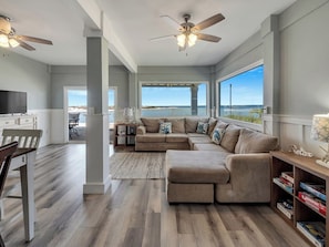 A spacious living room with a large sectional sofa, a television, and a bookshelf. - Navarre Beach Waterfront Home | Sleeps 22 | Gulf & Sound Views | Paradise Point (Navarre Beach)