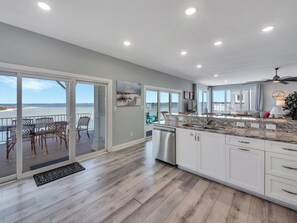 A modern kitchen with a view of the ocean, a dining area with outdoor seating, and a ceiling fan. - Navarre Beach Waterfront Home | Sleeps 22 | Gulf & Sound Views | Paradise Point (Navarre Beach)
