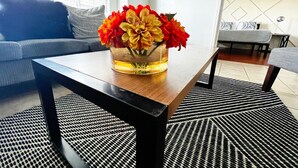 Ein Wohnzimmer mit Couch, Holz-Couchtisch, Blumenvase und einem gemusterten Teppich.