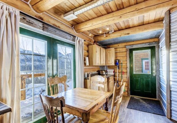 A wooden cabin interior with a dining area, kitchen, and a green door.