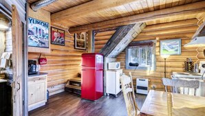 A log cabin interior with wooden walls, a red refrigerator, a white stove, and a dining table with chairs. - Log Cabin with Amazing Mountain & Lake Views  (allergy-friendly) (Carcross)