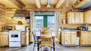 A wooden cabin interior with a dining table, chairs, a stove, and cabinets. - Log Cabin with Amazing Mountain & Lake Views  (allergy-friendly) (Carcross)