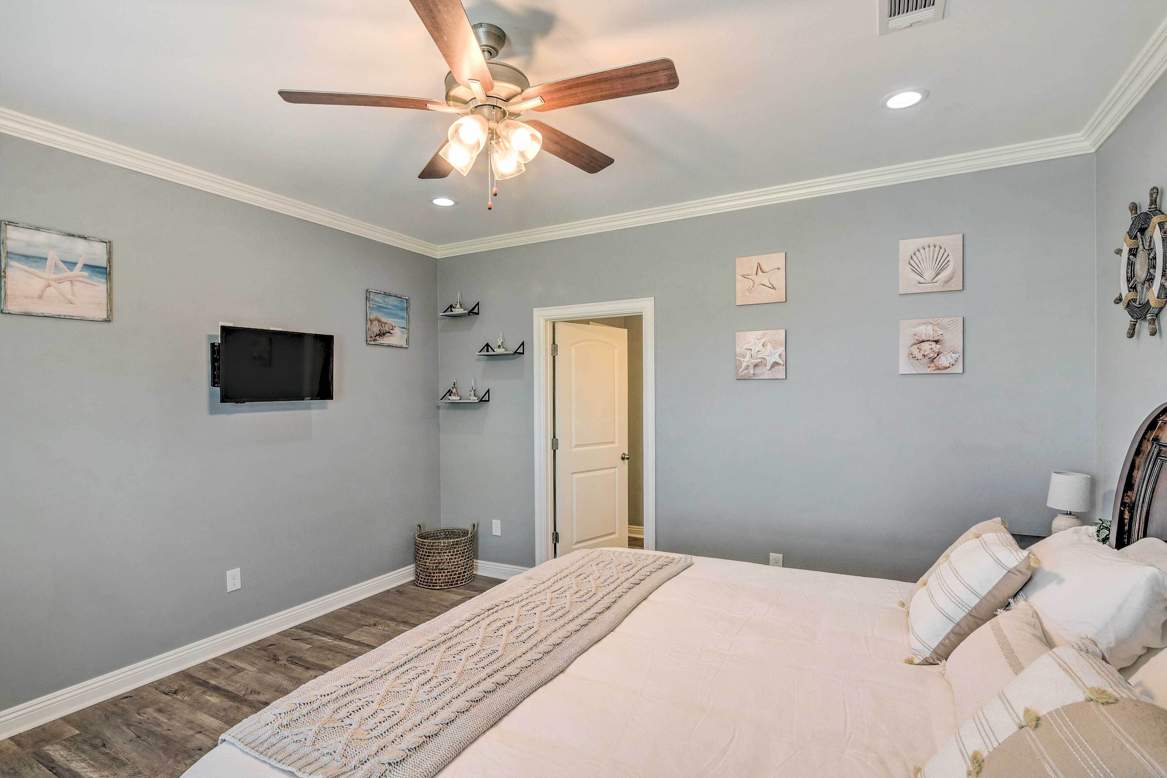 A bedroom with a bed, ceiling fan, wall-mounted TV, and nautical-themed decorations.