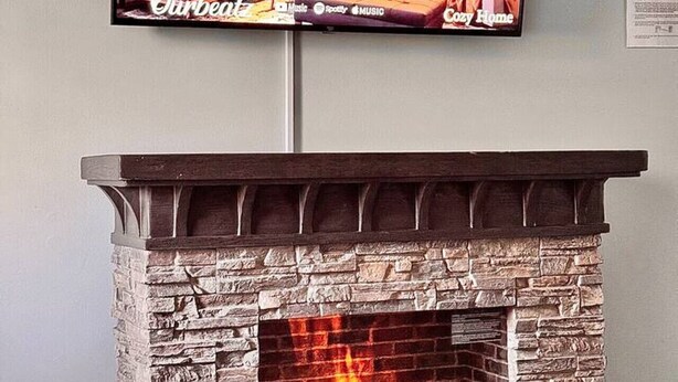A fireplace with a stone facade and a television mounted above it displaying a cozy living room scene. - Comfortable Open Space. Pets are allowed (Beaufort)