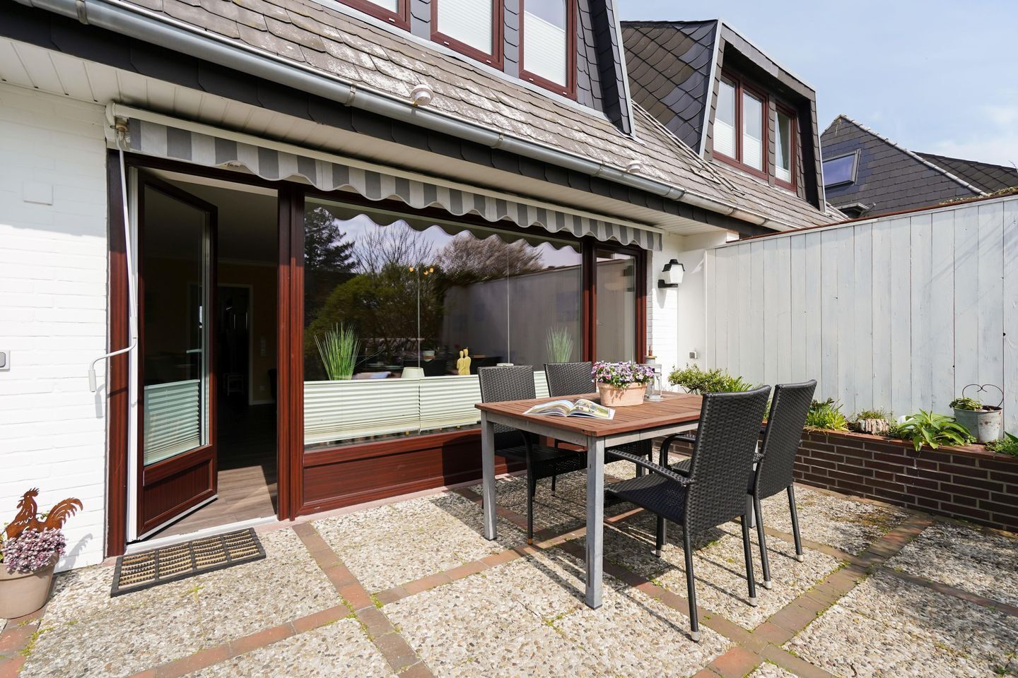 A patio with a table and chairs, a sliding glass door, and a garden area with plants.