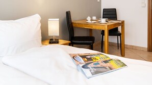 A hotel room with a bed, a nightstand with a lamp, a wooden table with chairs, and a magazine on the bed. - Adrian 5 - Simple, central apartment for 2 persons, incl. WLAN and TV, separate (Sylt)