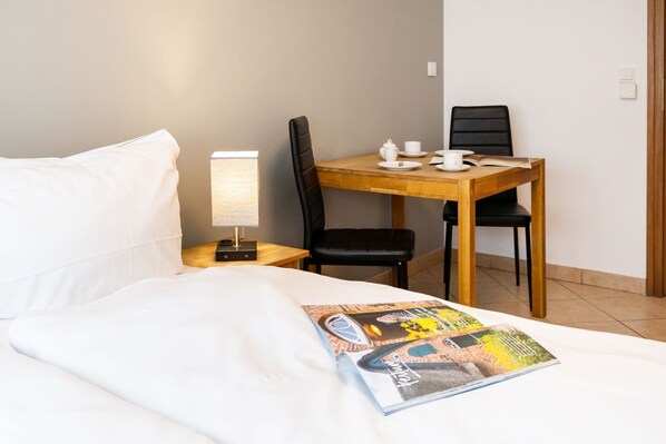 A hotel room with a bed, a nightstand with a lamp, a wooden table with chairs, and a magazine on the bed. - Adrian 5 - A simple, downtown apartment for 2 people, with Wi-Fi and a TV, self-contained (Sylt)