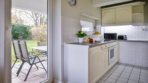 Una cocina con armarios blancos, un reloj, un microondas, un tostador y una ventana con vistas a un jardín.