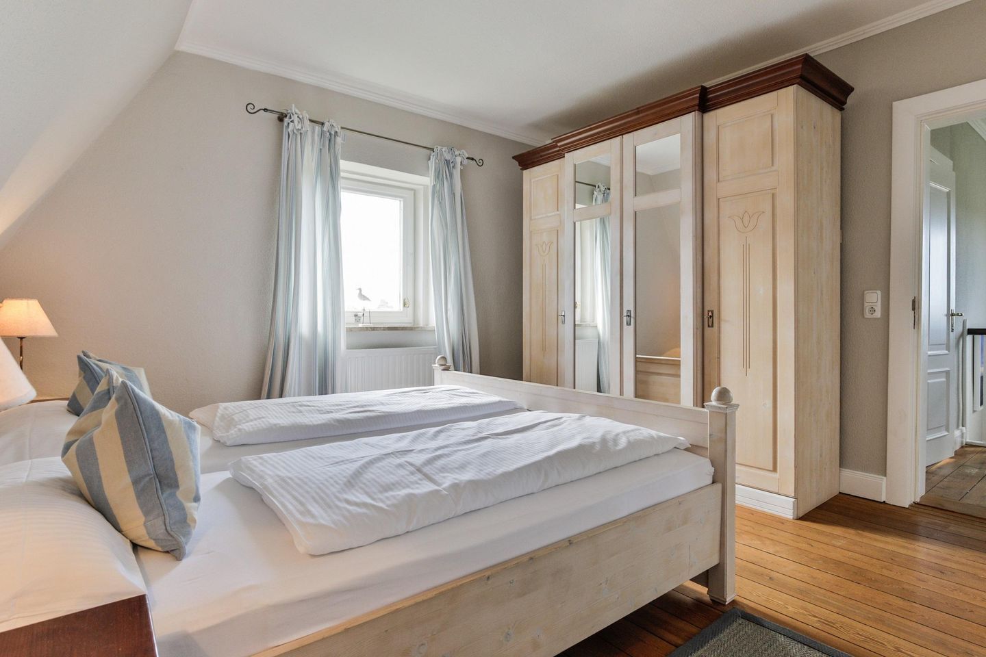 Een slaapkamer met een bed, nachtkastje, lamp, raam met gordijnen en een kledingkast.