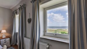 A bedroom with a view of the sea, a radiator, a bedside table with a lamp, and striped curtains. - Lena's Hüs - Beautiful thatched house for 6 pers. with sea view, garden, WLAN, (List)