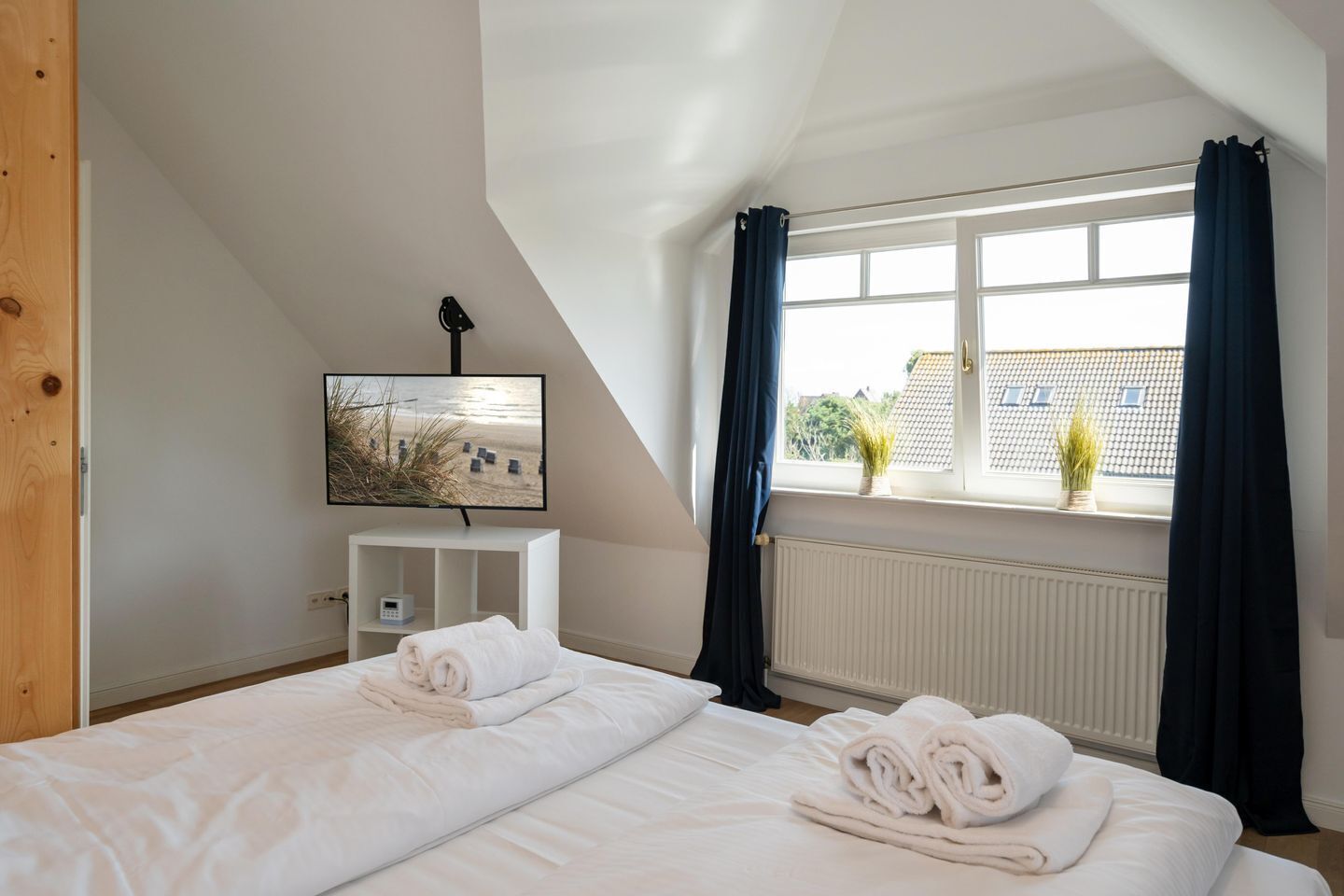 Ein Schlafzimmer mit zwei Betten, einem Fernseher auf einem Schrank, einem Fenster mit Vorhängen und Blick ins Freie.