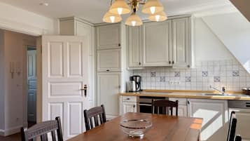 A modern kitchen with white cabinetry, a wooden dining table, and a chandelier.