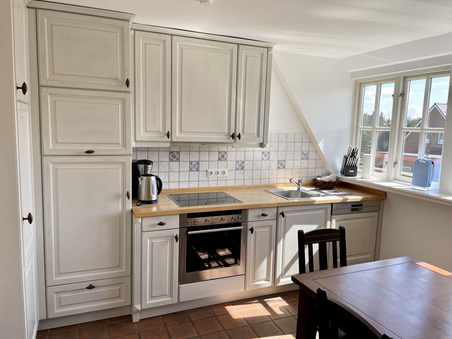 A kitchen with white cabinets, a stove, an oven, a sink, and a window with a view of the outside.