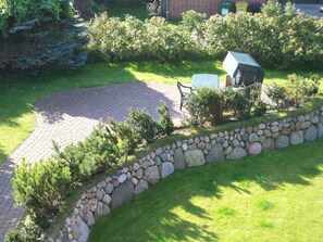 A garden with a paved area, stone wall, and outdoor furniture. - Min Hüs OG - Apartment close to the beach for 6 pers. with sauna, terrace, WLAN. Pets (Sylt)