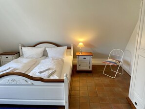 A neatly made bed with white linens and pillows, a bedside lamp, a chair, and a small nightstand. - Min Hüs OG - Apartment close to the beach for 6 pers. with sauna, terrace, WLAN. Pets (Sylt)