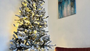 Ein Weihnachtsbaum mit Lichterketten, ein braunes Ledersofa und ein Gemälde an der Wand.