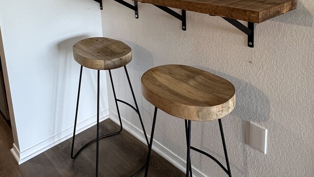 Eine Küche mit einer Holzausziehtheke, zwei Hocker, einer Topfpflanze und einem runden Spiegel an der Wand.