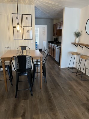 A modern kitchen with wooden cabinets, a dining area with a table and chairs, and a hallway leading to a living space. - Little Gem : 3 bedroom : Balcony : Pool Open : Sleeps 8 : 2 baths (Branson)