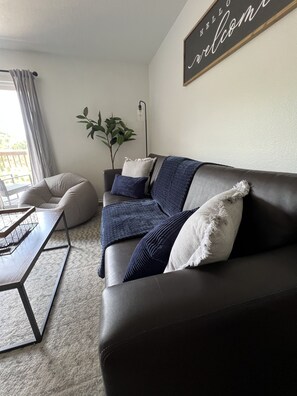 A modern living room with a dark leather sofa, a coffee table, and a plant. - Little Gem : 3 bedroom : Balcony : Pool Open : Sleeps 8 : 2 baths (Branson)