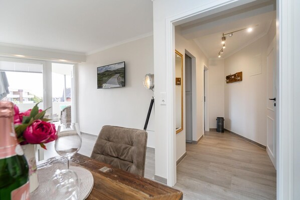Un comedor moderno con una mesa de madera, una silla y un jarrón de flores. Hay un cuadro en la pared y un pasillo que conduce a otra habitación.