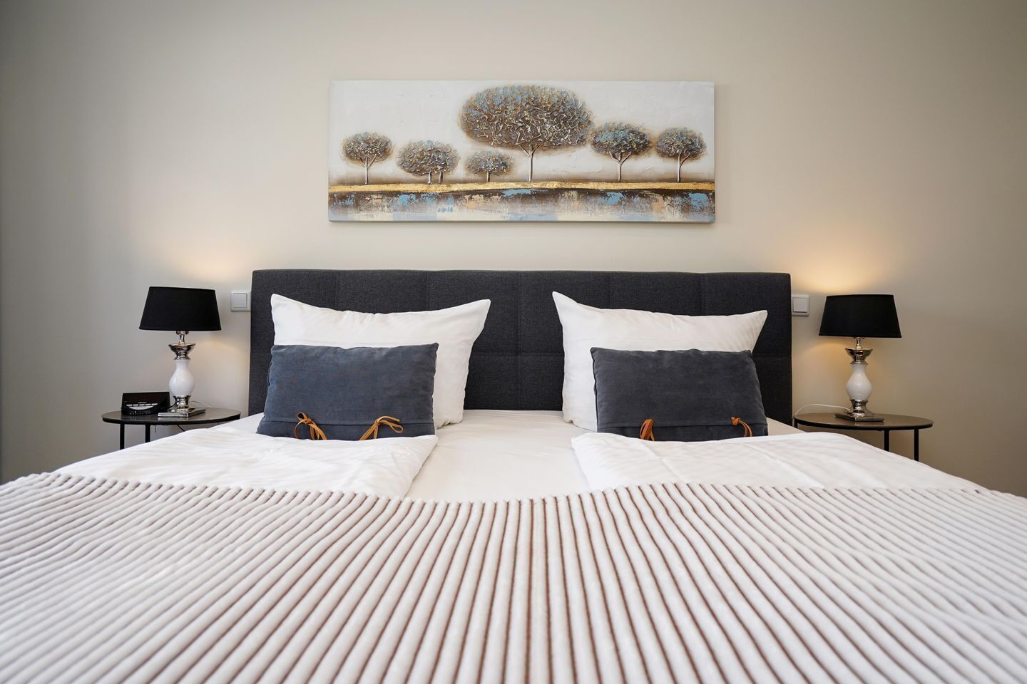 A neatly made bed with a striped white duvet, two pillows, and two bedside tables with lamps.