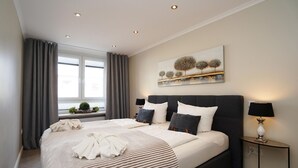 Ein modernes Schlafzimmer mit einem großen Bett, einem dunklen Kopfteil und einem Nachttisch mit Lampe.