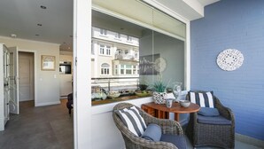 Ein Balkon mit Korbstühlen, einem Tisch und Blick auf ein Gebäude durch eine Glastür.