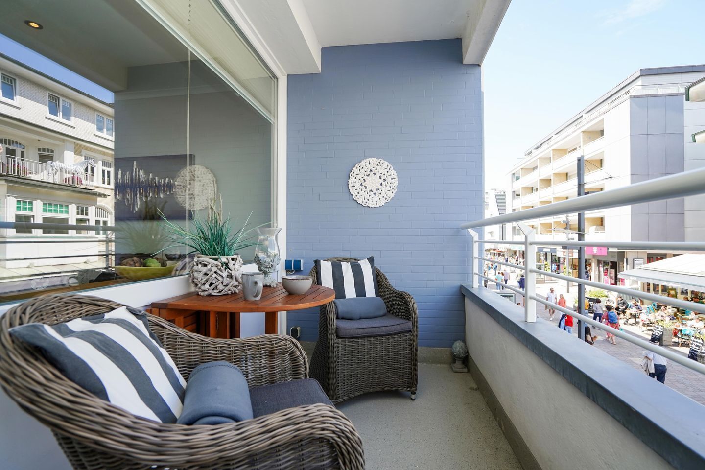 Een balkon met rieten meubels, een tafel met decoratieve objecten en uitzicht op een drukke straat en gebouwen.