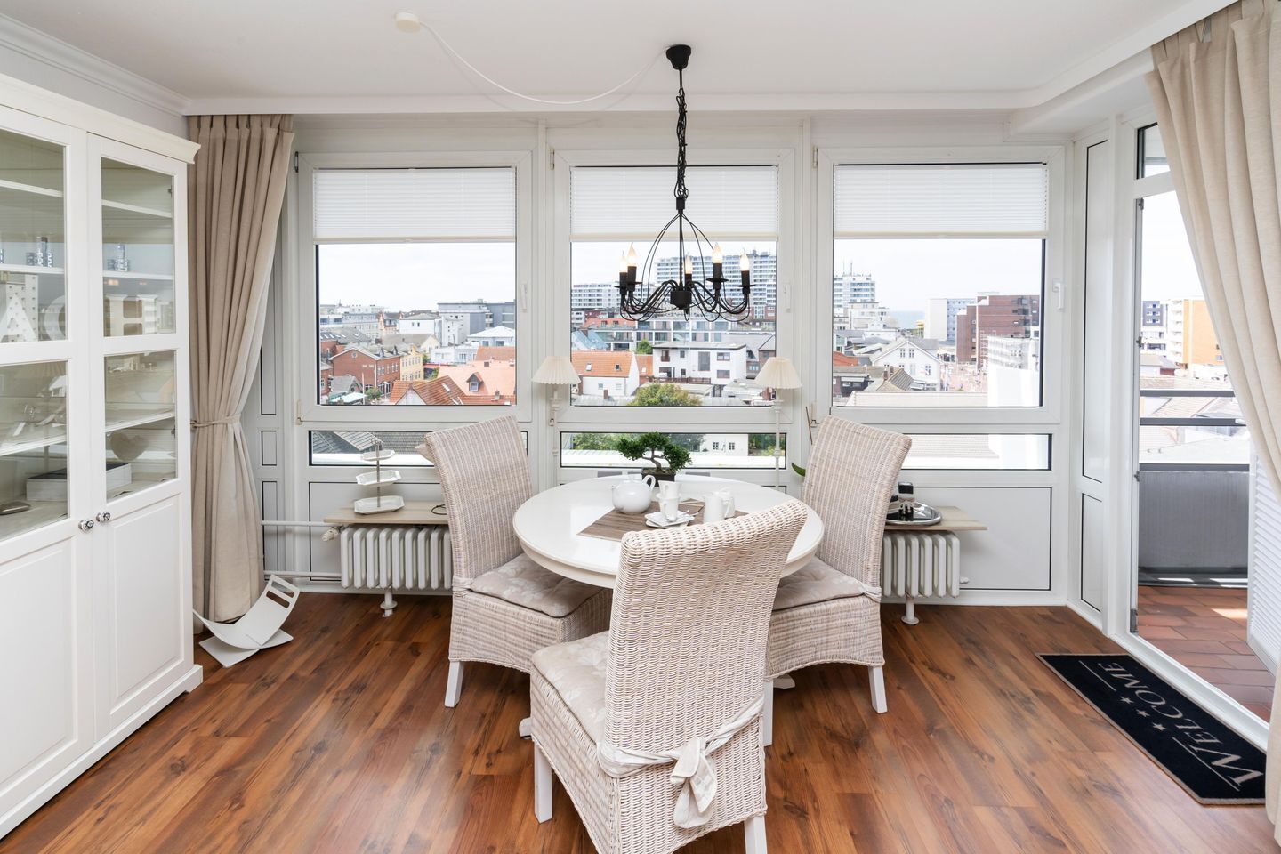 Ein Essbereich mit einem runden Tisch, Korbstühlen und Blick auf die Stadt durch große Fenster.