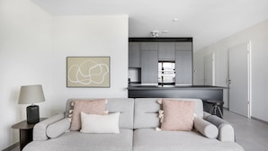 Un moderno salón con un sofá gris, una lámpara y una cocina al fondo.