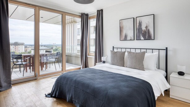 Un dormitorio moderno con una cama grande, un balcón con mobiliario exterior y dos cuadros enmarcados en la pared.