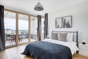 Un dormitorio moderno con una cama grande, un balcón con mobiliario exterior y dos cuadros enmarcados en la pared.