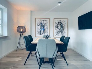 Une salle à manger moderne avec une table ronde, six chaises, deux tableaux abstraits encadrés, un lampadaire et un téléviseur à écran plat fixé au mur.