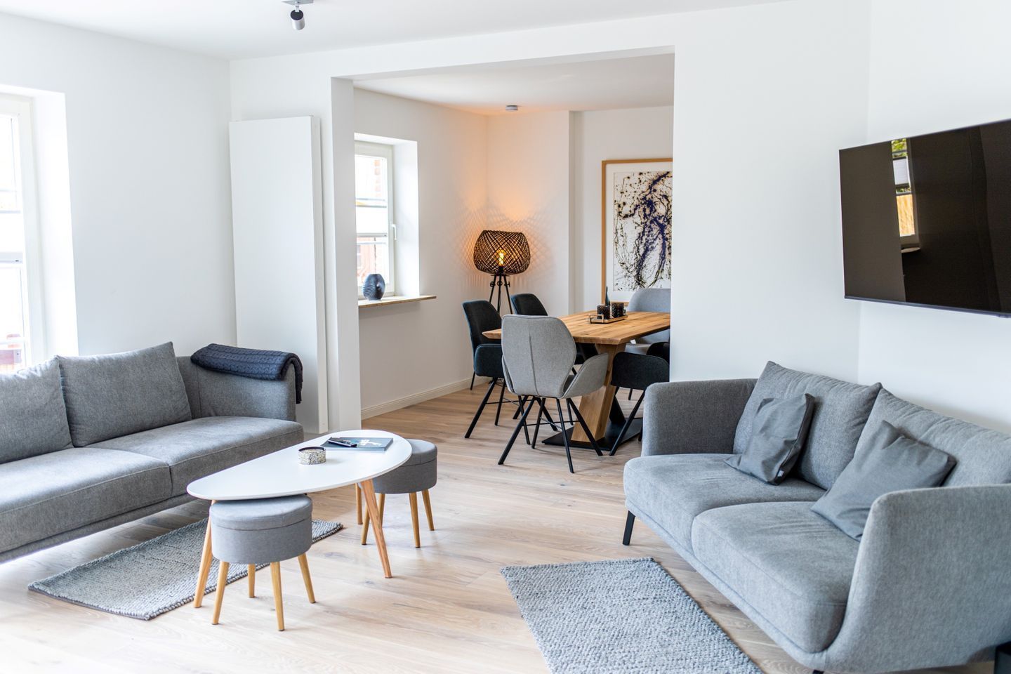 Una sala de estar moderna con sofás grises, una mesa de centro redonda y un comedor con sillas y una mesa.