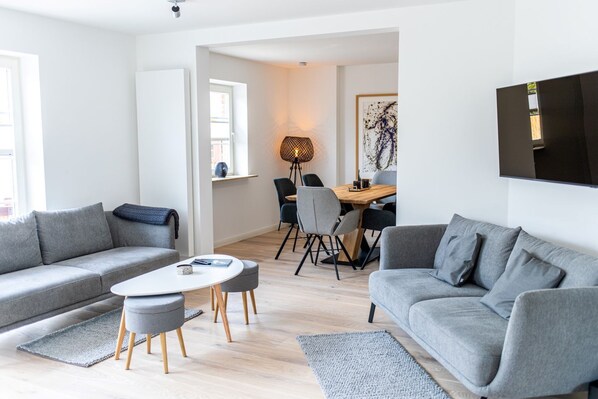 Una sala de estar moderna con sofás grises, una mesa de centro redonda y un comedor con sillas y una mesa.