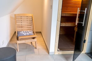 Una silla de madera con cojín en una habitación con suelo de baldosas y una puerta de madera que da a un altillo.