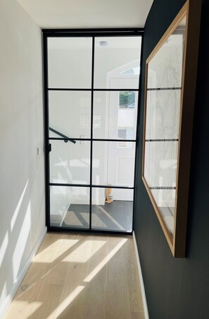 Une pièce dotée d’une porte-fenêtre coulissante donnant sur un balcon, d’une œuvre d’art encadrée au mur et d’un plancher en bois.