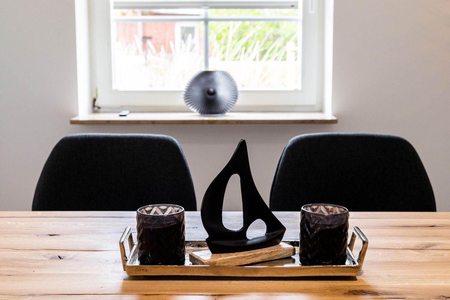 Une table en bois, avec deux verres foncés et une sculpture abstraite noire.
