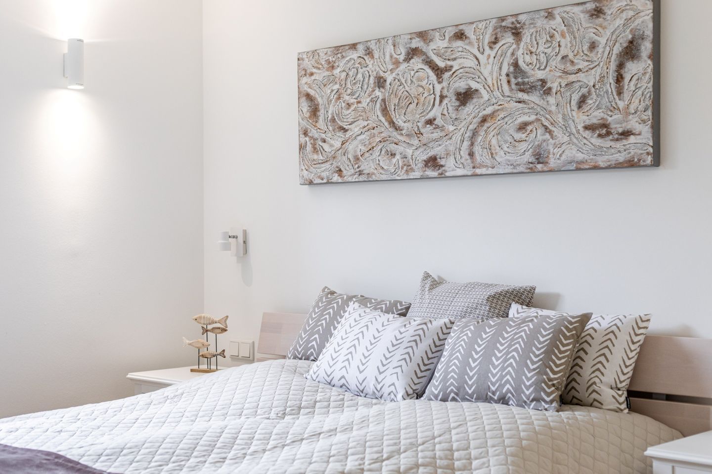 Une chambre à coucher bien rangée, avec un lit, des oreillers, une œuvre d’art accrochée au mur et des lampes de chevet.