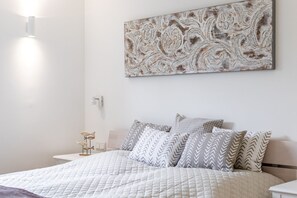 Une chambre à coucher bien rangée, avec un lit, des oreillers, une œuvre d’art accrochée au mur et des lampes de chevet.